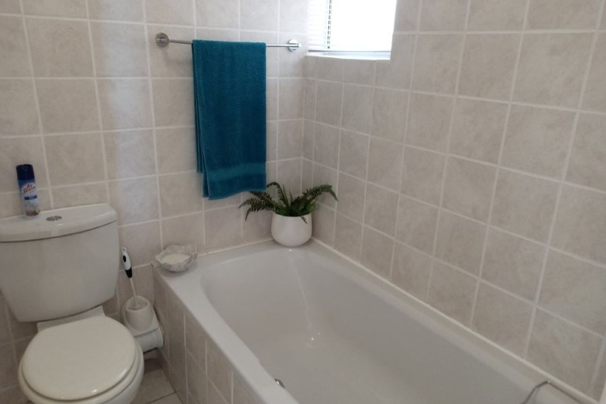 A functional bathroom featuring a built-in bathtub, ceramic wall tiling, and a standard toilet suite.