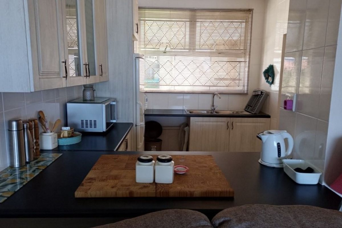 A functional kitchen featuring laminate cabinetry, dark countertops, a double basin sink, and tiled backsplash with natural light from a window.