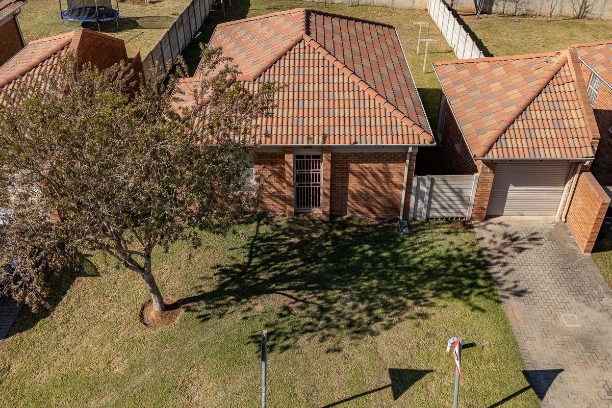 Aerial view of a residential property featuring a brick facade, tiled roof, paved driveway, and a single garage.
