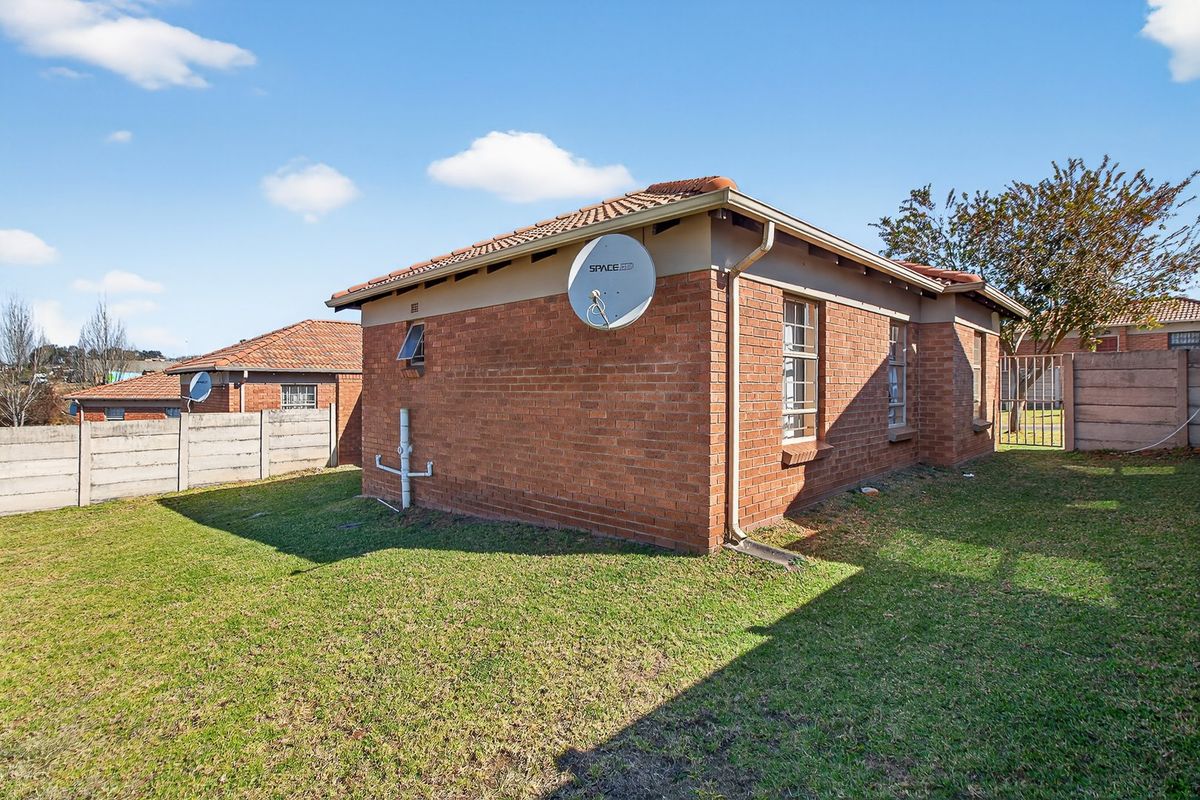 Rear view of the face brick house featuring a tiled roof, satellite dish, and a private garden enclosed by precast concrete boundary walls.