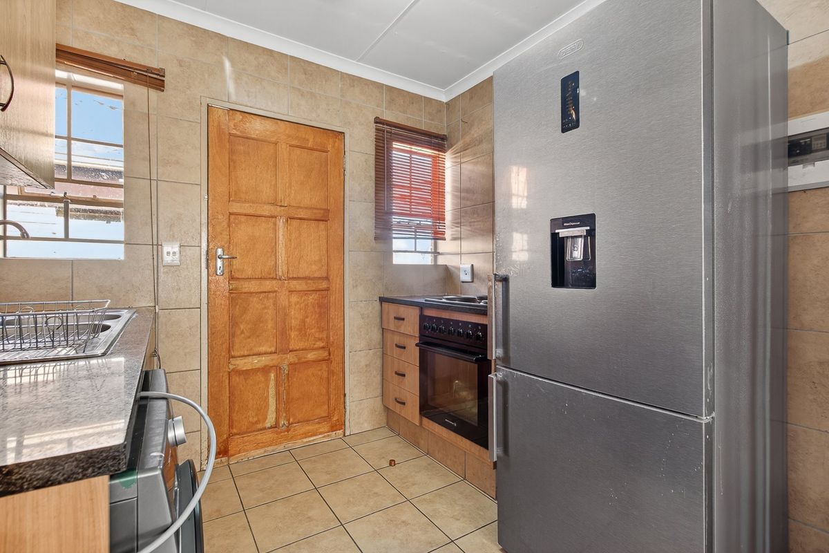 A functional kitchen featuring tiled walls and flooring, built-in oven and hob, and a wooden exterior door.