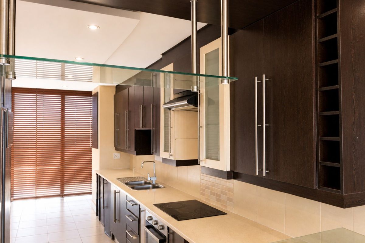 Modern kitchen featuring dark wood cabinetry, stone countertops, integrated appliances, and a sleek tiled backsplash with recessed lighting.