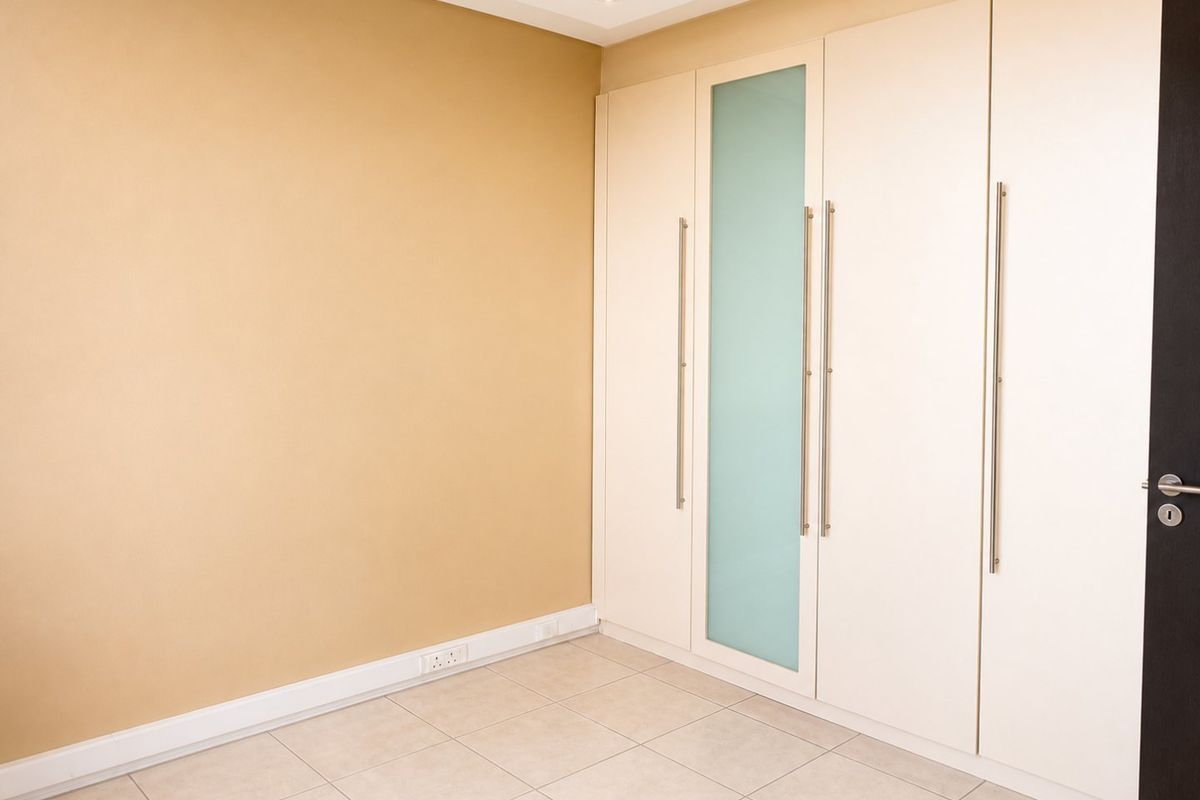 A clean, empty bedroom featuring neutral walls, tiled flooring, and modern built-in cupboards with a frosted glass accent panel.