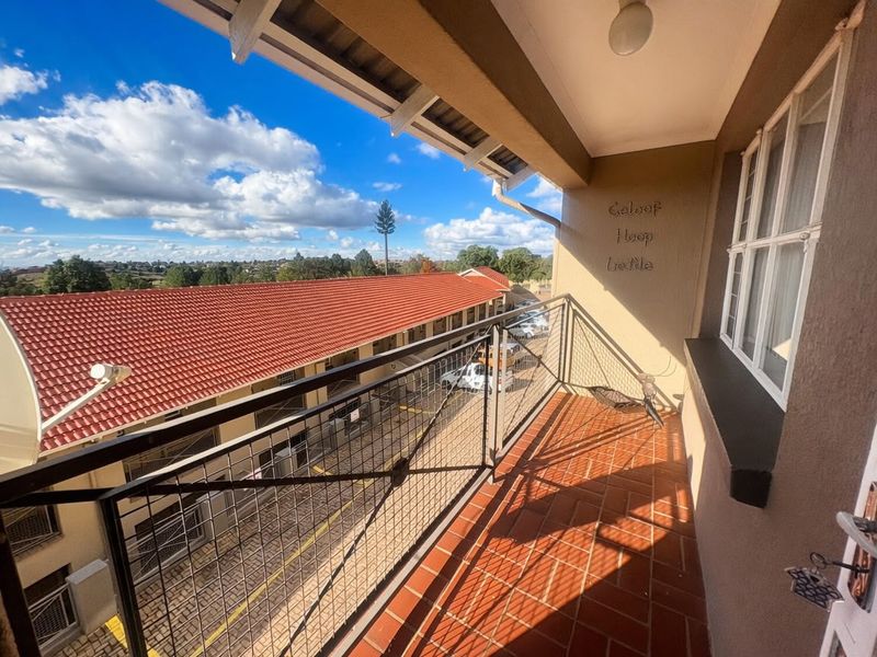 A covered balcony featuring terracotta tiling and a metal balustrade, offering an elevated view of the complex grounds and surrounding area.