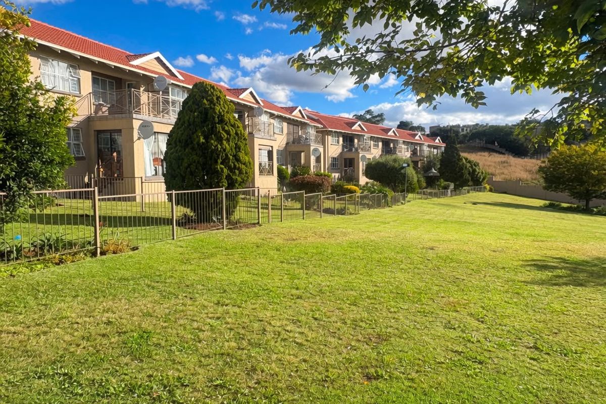 A view of the rear elevation of the apartment complex, featuring balconies, tiled roofing, and a well-maintained communal lawn area.