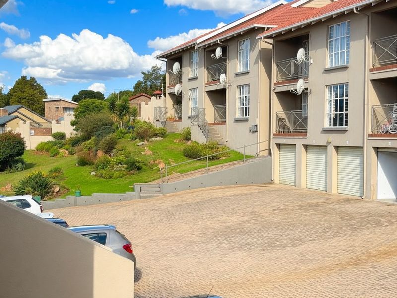 Exterior view of a multi-story apartment complex featuring paved driveway access, integrated garages, and private balconies with landscaped garden surroundings.