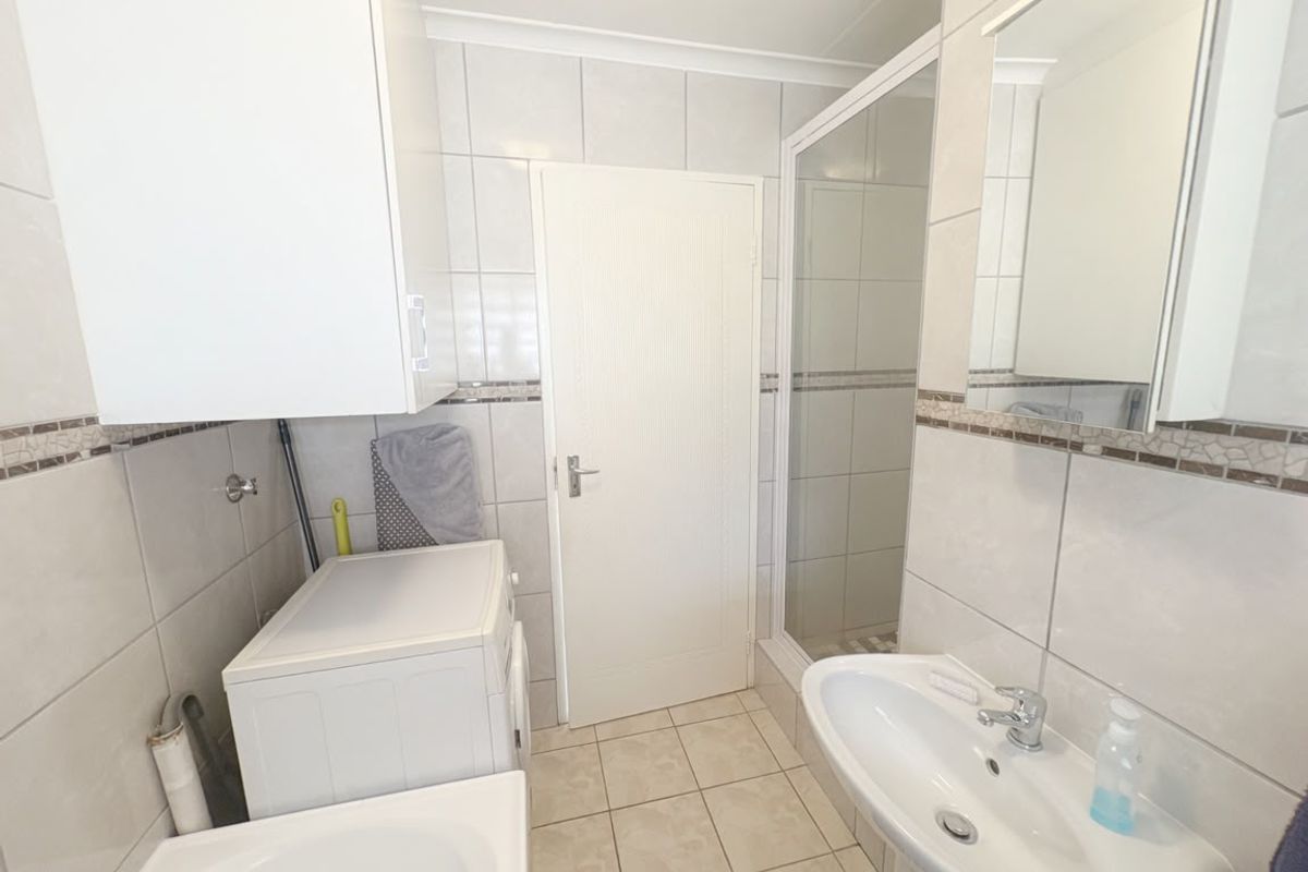 A functional bathroom featuring a pedestal basin, shower enclosure, and wall-mounted cabinetry with neutral tiled finishes throughout.