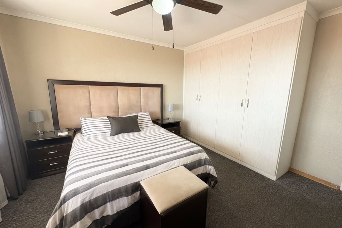 A well-maintained bedroom featuring neutral walls, dark carpeting, and ample built-in cupboard storage space.