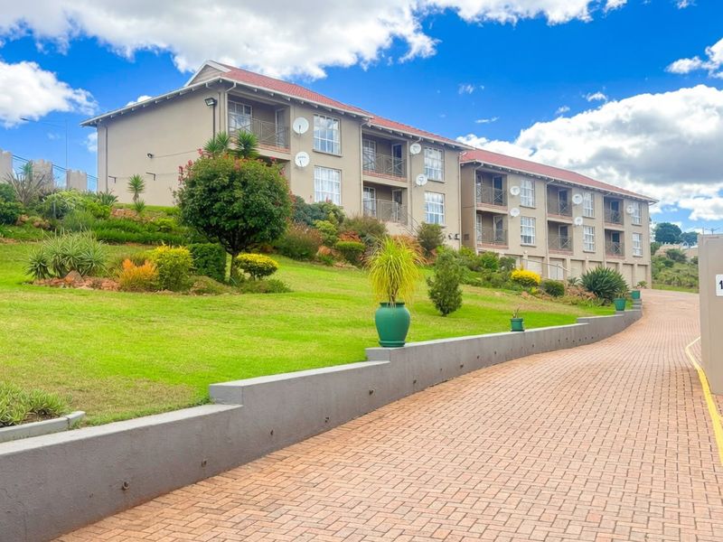 A well-maintained apartment complex featuring a paved driveway, landscaped garden, and private balconies for each unit under a tiled roof.