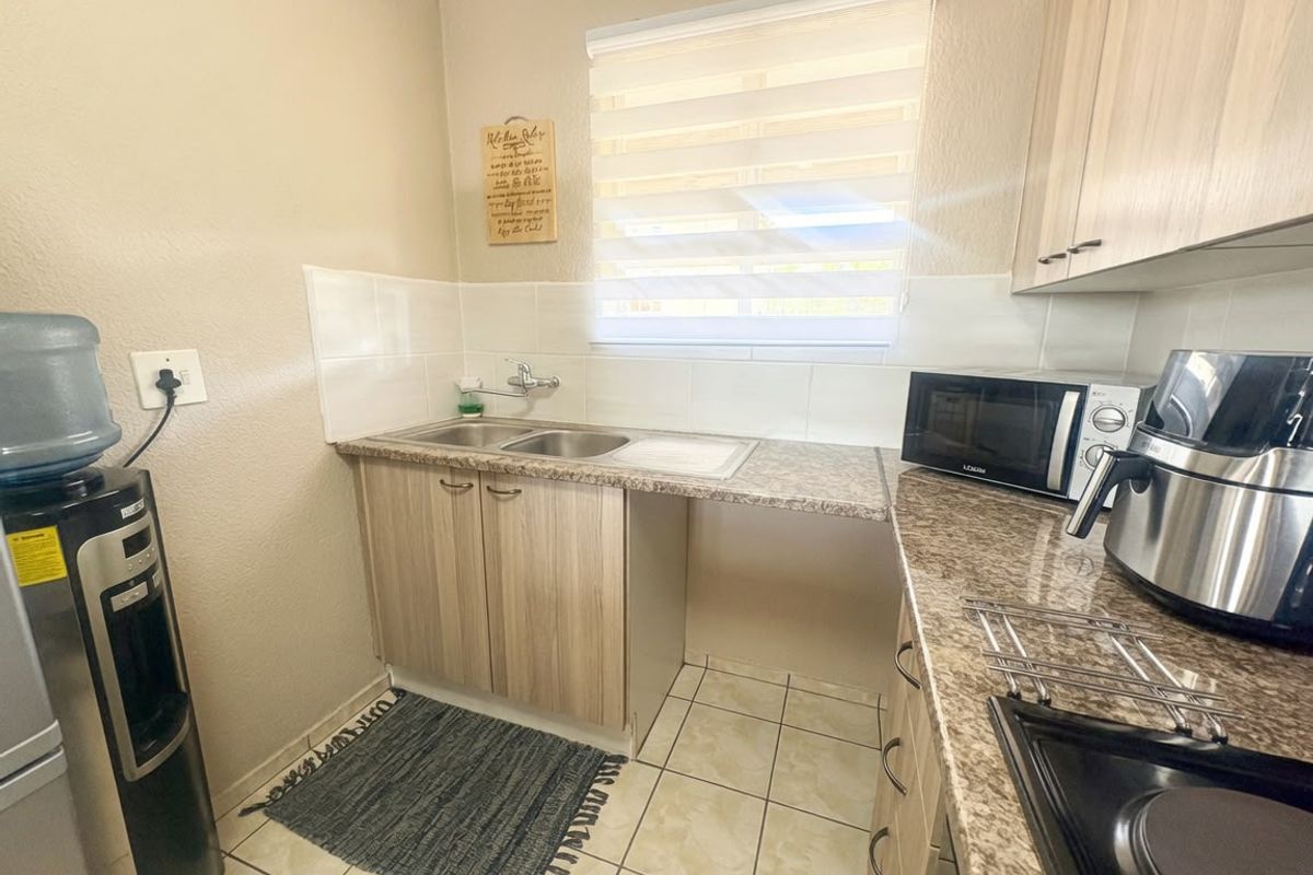 Compact kitchen featuring laminate cabinetry, granite-look countertops, a double bowl stainless steel sink, and tiled splashbacks with neutral wall finishes.