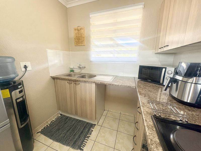 Compact kitchen featuring laminate cabinetry, granite-look countertops, a double bowl stainless steel sink, and tiled splashbacks with neutral wall finishes.