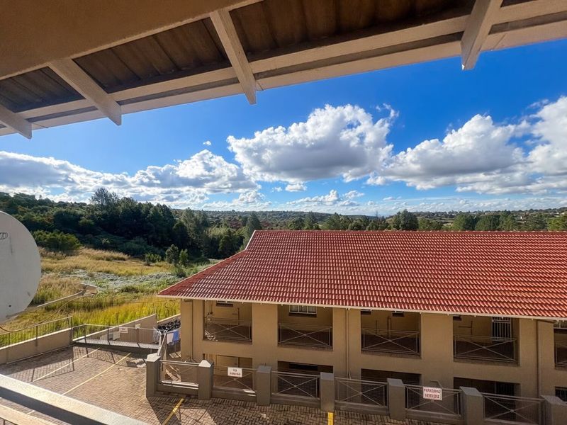 Elevated view overlooking a neighbouring apartment complex with terracotta roof tiles and surrounding natural landscape.