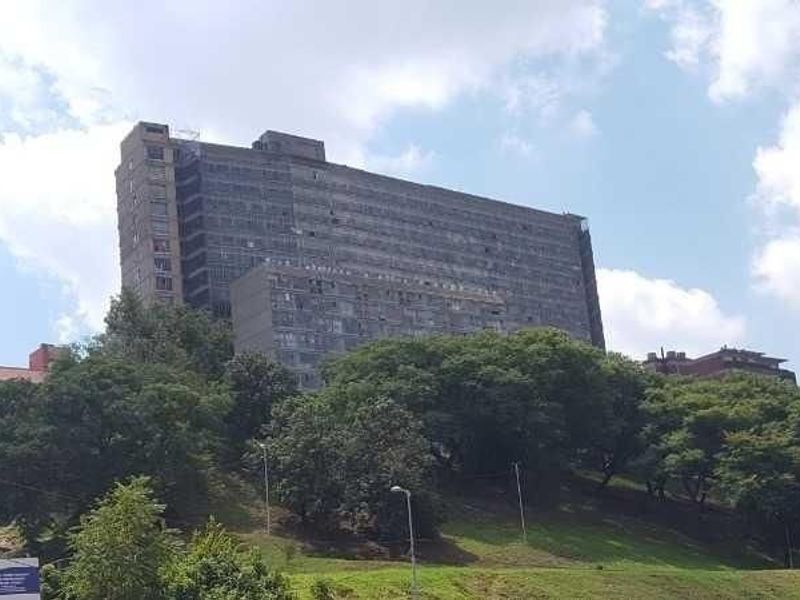A view of a large multi-story apartment building situated on a landscaped hill, showcasing the exterior facade and surrounding greenery.