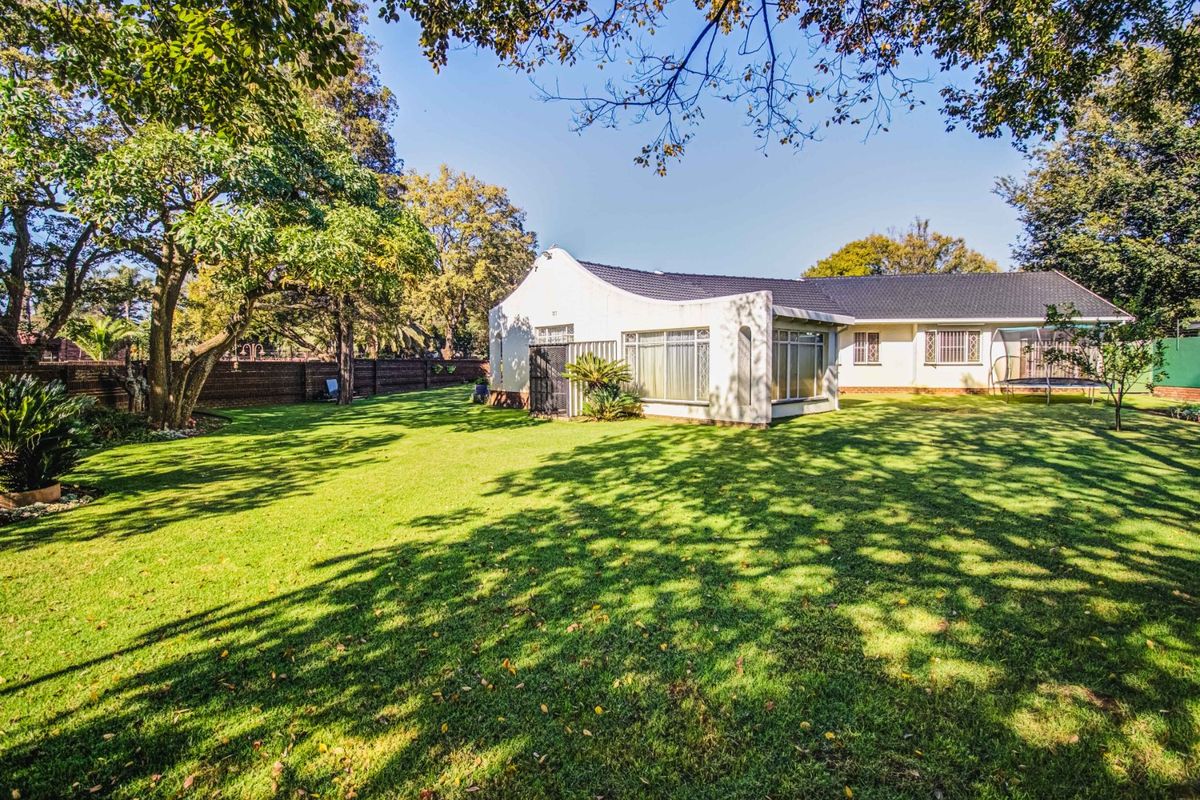 A view of the rear elevation of the house featuring a well-maintained lawn, mature trees, and secure boundary walls.