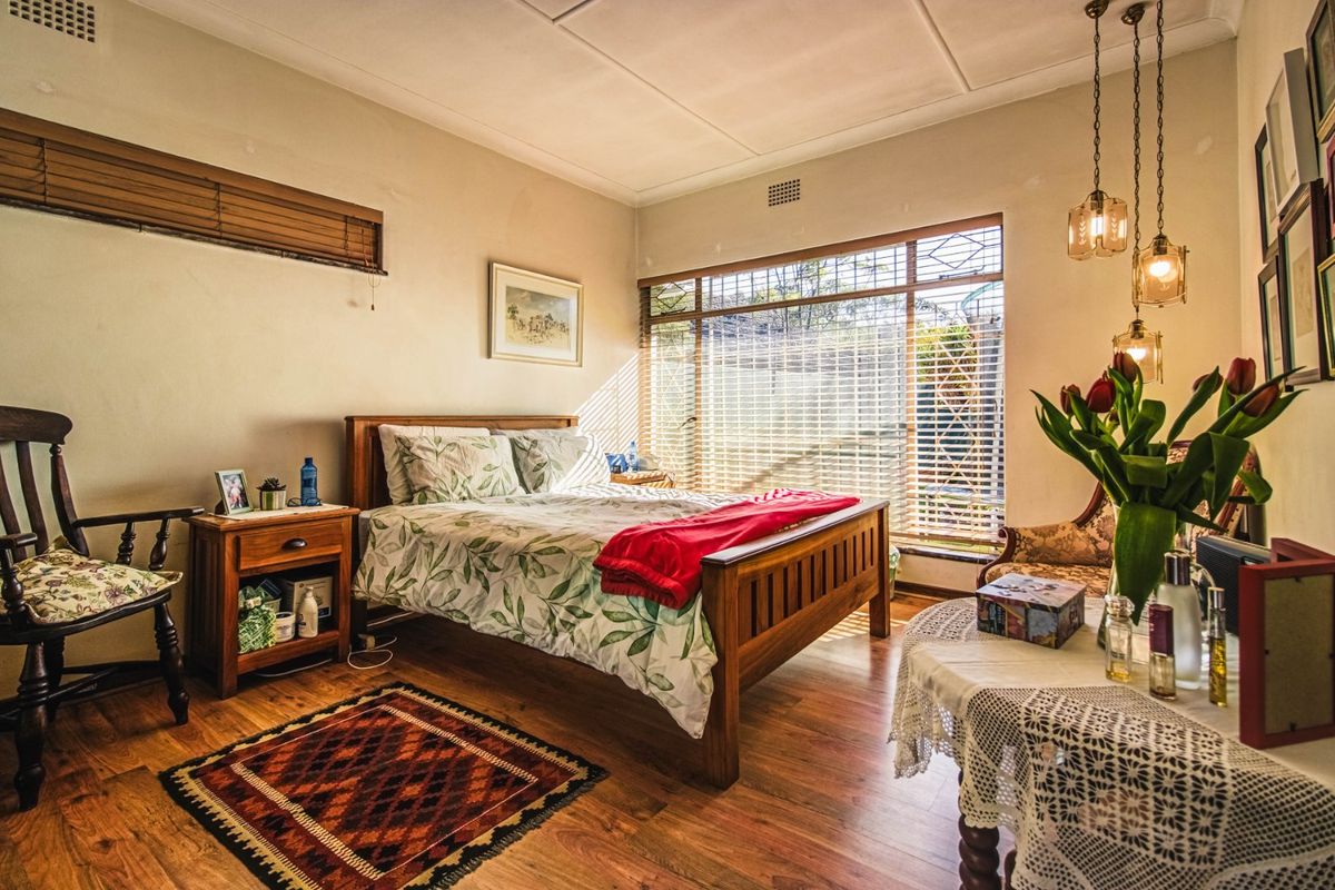 A cozy bedroom featuring laminate flooring, large windows with security bars, and pendant lighting, offering a comfortable and functional living space.
