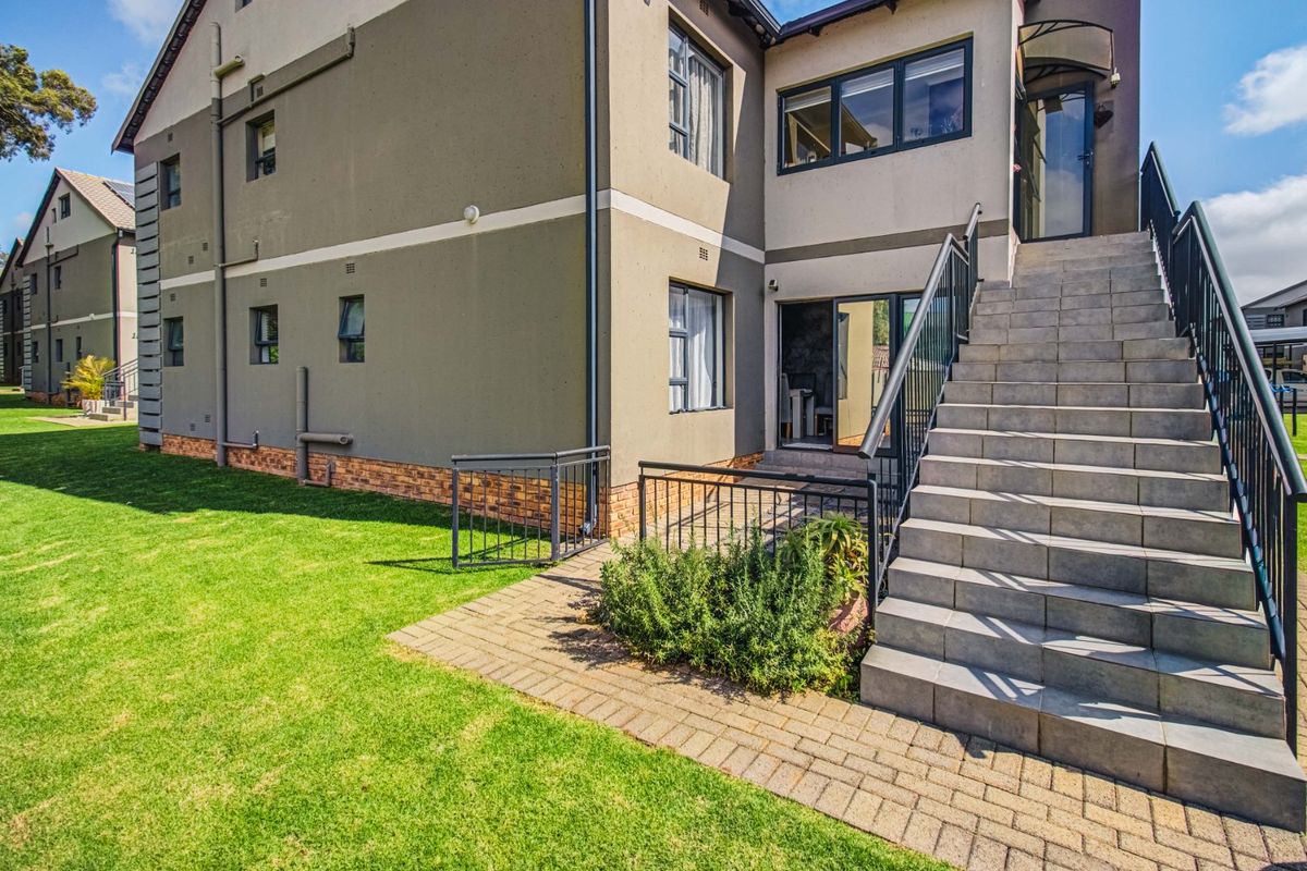 Rear exterior view of the townhouse featuring a tiled staircase with metal balustrades, paved walkway, and well-maintained lawn area.