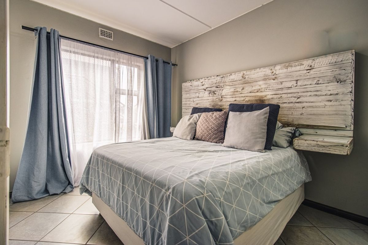 A bedroom featuring tiled flooring and a ventilation grille, with natural light entering through a window.