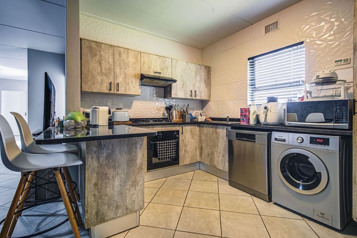 A functional kitchen featuring wood-look laminate cabinetry, granite countertops, a breakfast bar, and integrated appliances including an oven and hob.