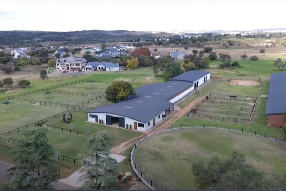 Aerial view of a residential equestrian property featuring stables, paddocks, and landscaped grounds in a rural estate setting.