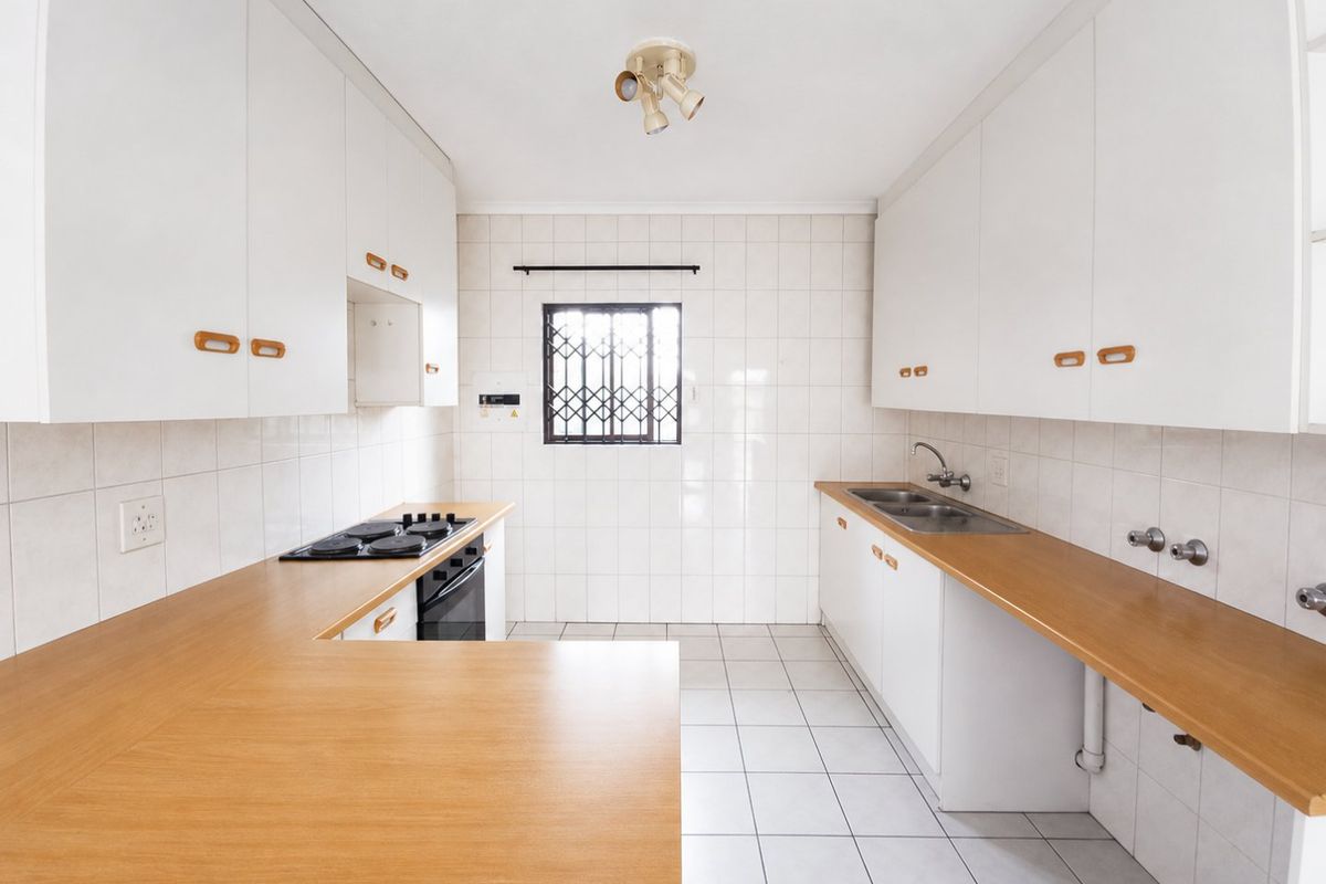 A functional, empty kitchen featuring white cabinetry, laminate countertops, a built-in oven and hob, and tiled finishes throughout.