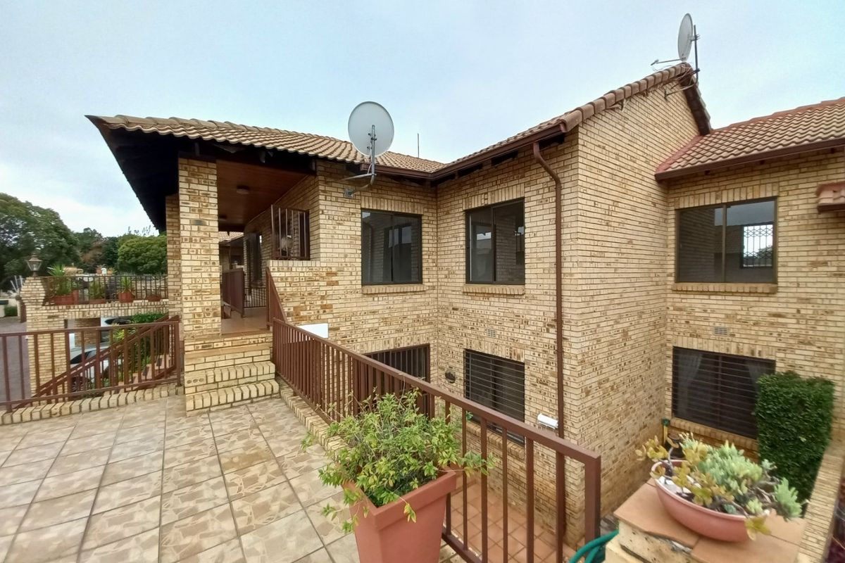 Rear exterior view of a face brick townhouse featuring a tiled patio, metal balustrades, and security bars on windows.