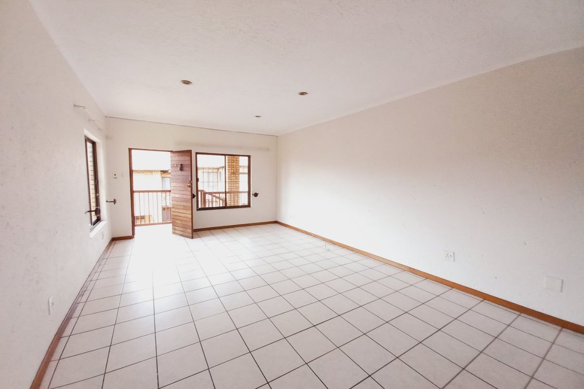 A bright, empty living area featuring neutral tiled flooring, recessed lighting, and direct access to an outdoor balcony through a timber door.