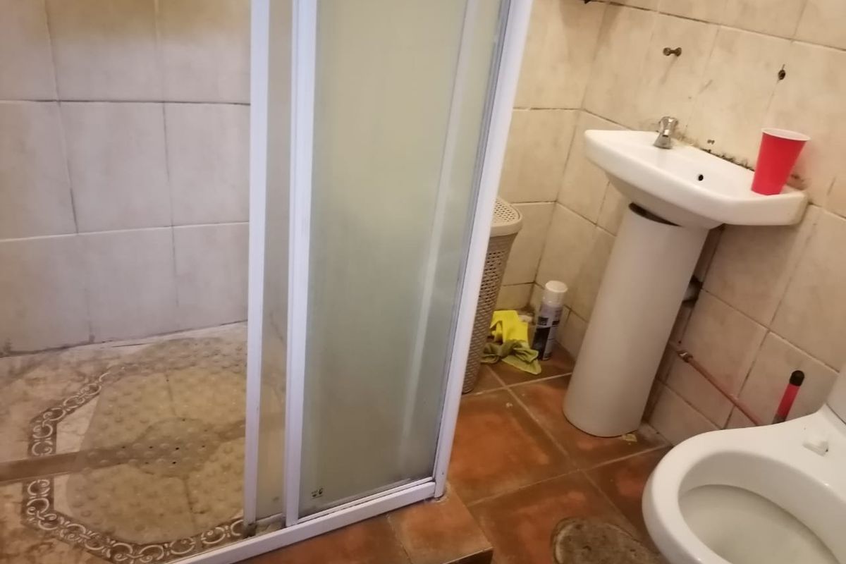 A dated bathroom featuring a shower enclosure, pedestal basin, and toilet, requiring significant renovation and cosmetic updates to improve its condition.