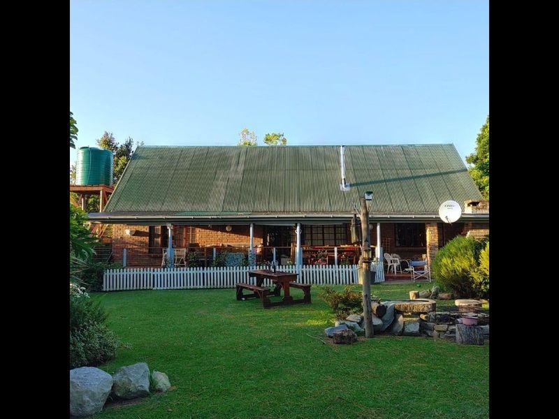 Rear view of a brick house featuring a corrugated metal roof, a covered patio area, and a spacious garden with a water tank.