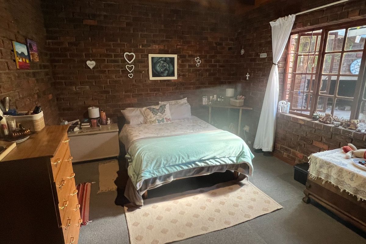 A bedroom featuring rustic exposed brick walls, timber ceiling beams, and a timber-framed window, offering a cozy and character-filled living space.
