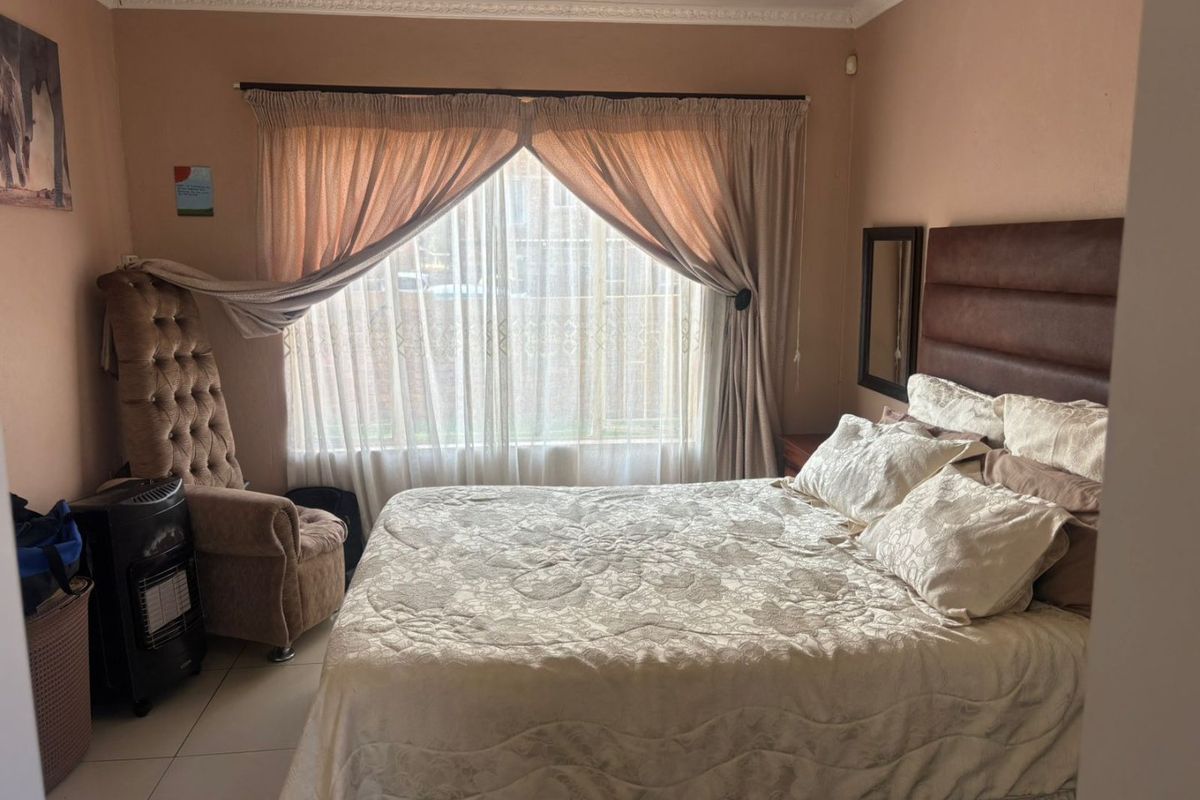 A bedroom featuring tiled flooring, decorative ceiling cornicing, and a large window with curtain treatments.