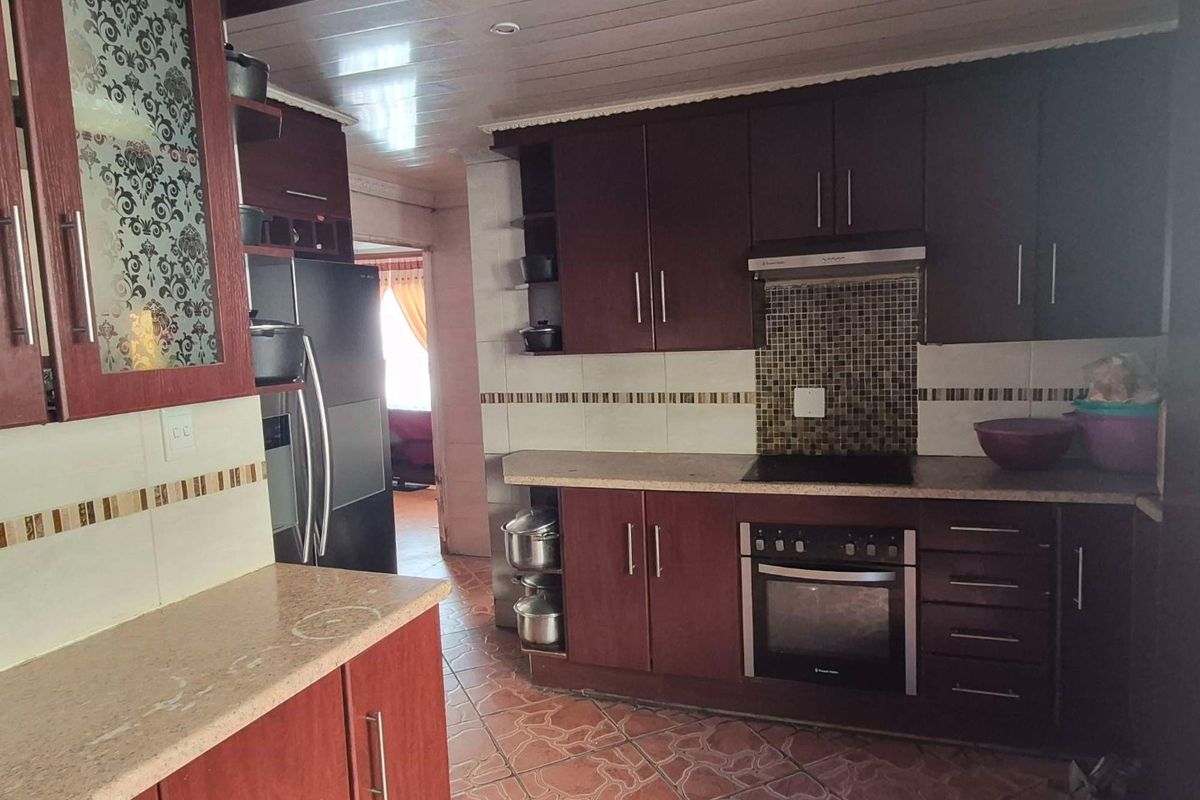 A functional kitchen featuring dark wood cabinetry, mosaic tile backsplash, built-in oven and hob, and ceramic floor tiles.