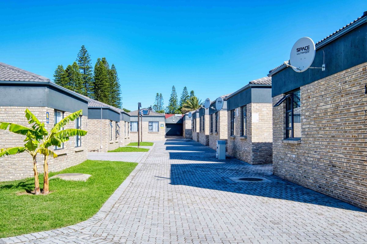 A view of the townhouse complex exterior featuring brick facades, paved driveways, and well-maintained lawn areas under a clear blue sky.