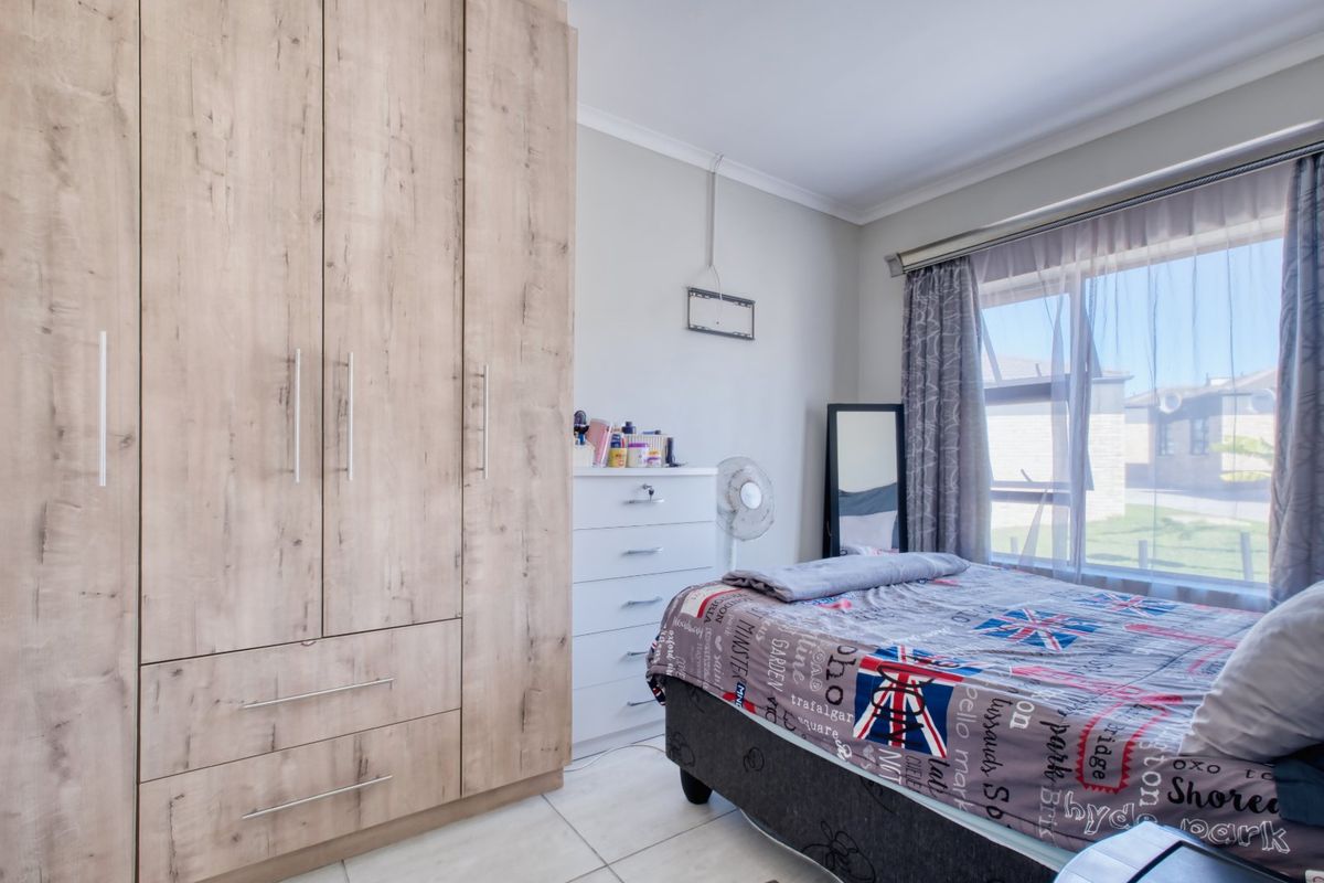 A well-maintained bedroom featuring light wood-grain built-in wardrobes, tiled flooring, and large windows allowing for natural light.