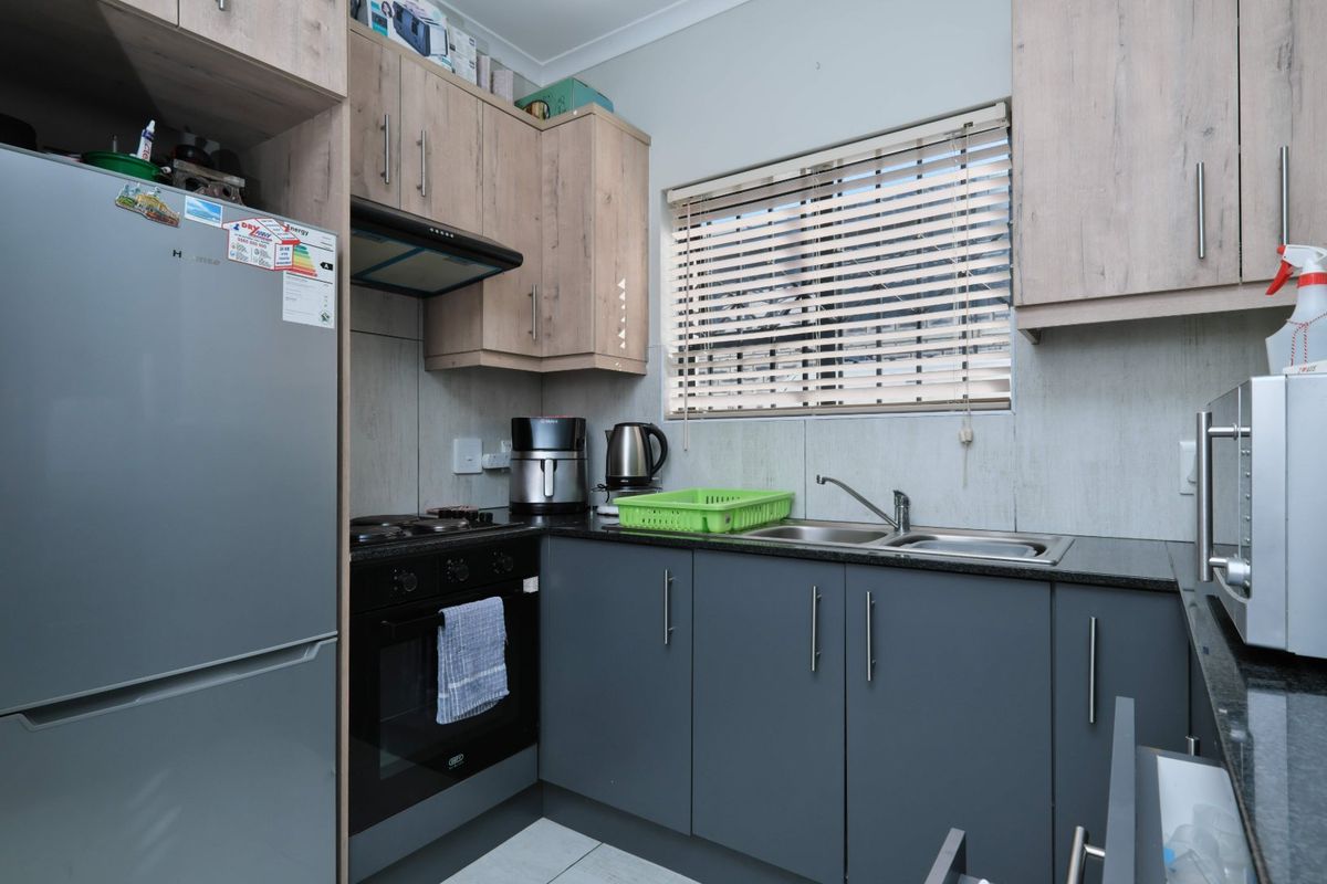 Compact kitchen featuring modern two-tone cabinetry, granite-look countertops, a stainless steel double sink, and integrated cooking appliances.