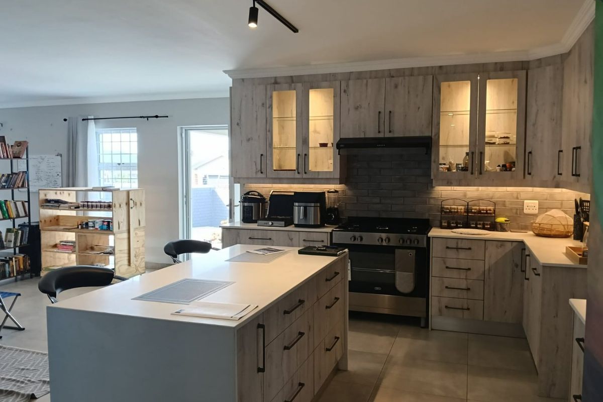 Modern kitchen featuring light wood-grain cabinetry, a central island, built-in gas stove with extractor, and integrated under-cabinet lighting.