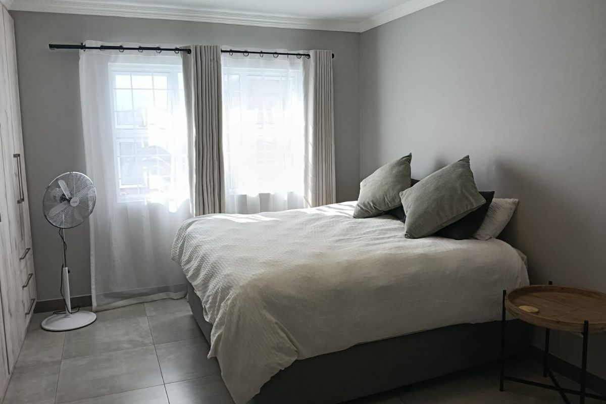 A well-maintained bedroom featuring neutral grey walls, large format floor tiles, and a built-in wardrobe with modern finishes.