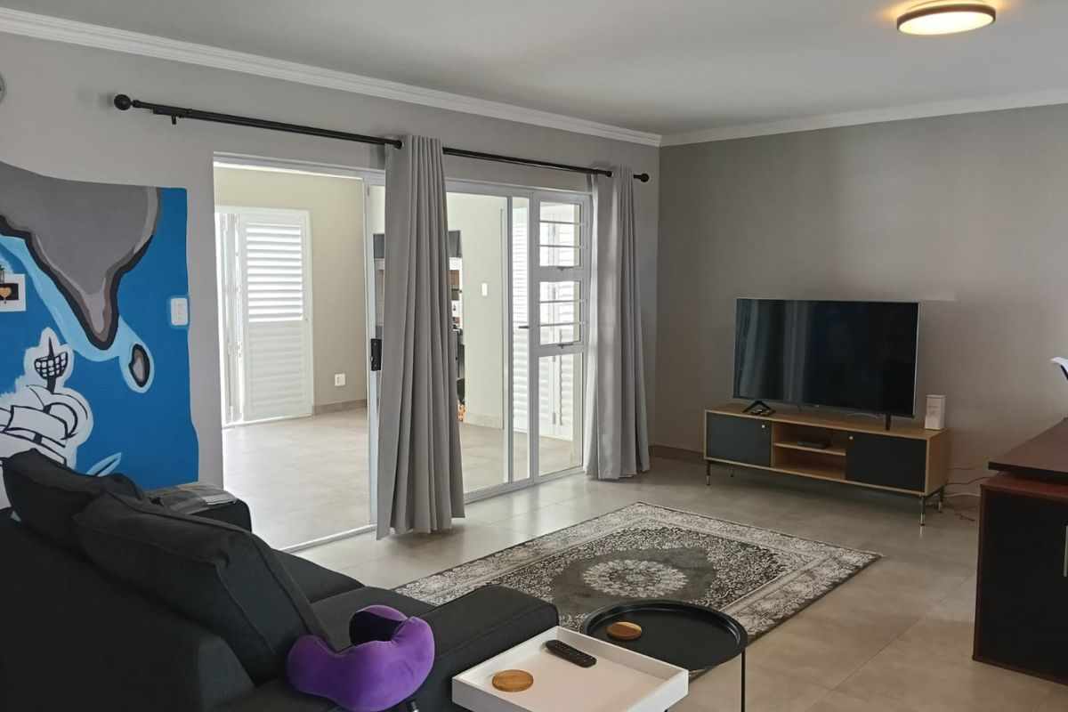 A well-maintained living room featuring neutral tiled flooring, modern ceiling lighting, and large sliding glass doors providing access to an adjacent outdoor space.