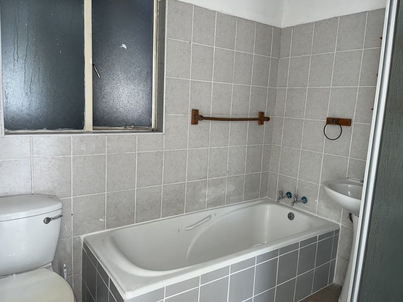 A functional bathroom featuring a bathtub, pedestal sink, and toilet with neutral wall tiling, requiring cosmetic updates to refresh the space.