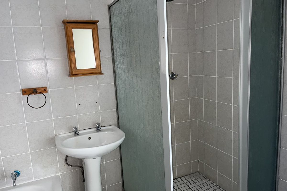 A functional bathroom featuring a pedestal basin, a separate shower enclosure with tiled walls, and basic sanitary fixtures.
