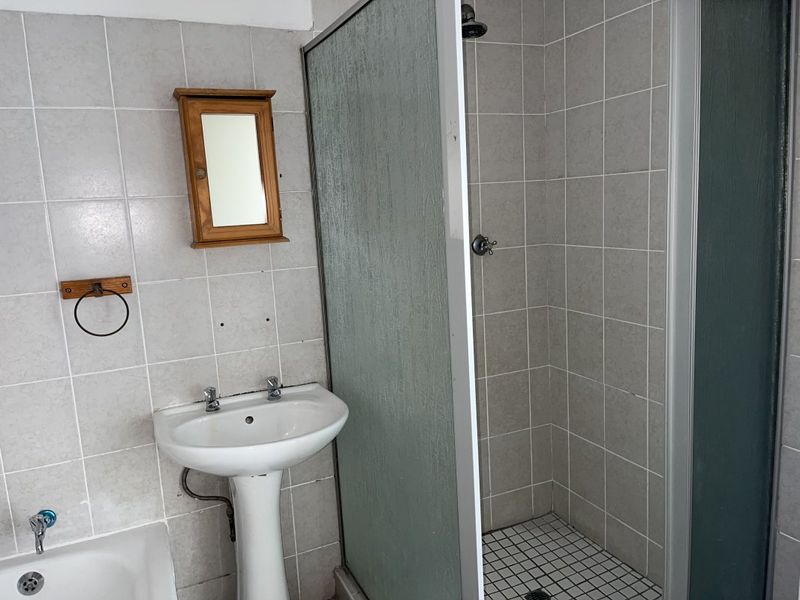 A functional bathroom featuring a pedestal basin, a separate shower enclosure with tiled walls, and basic sanitary fixtures.