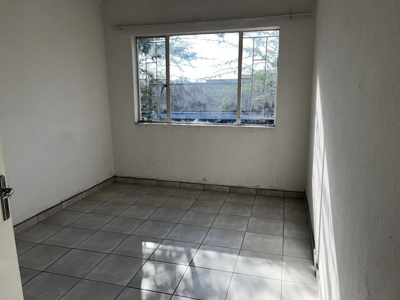 An empty bedroom featuring tiled flooring, a window with security bars, and a curtain rail, ready for a fresh coat of paint.