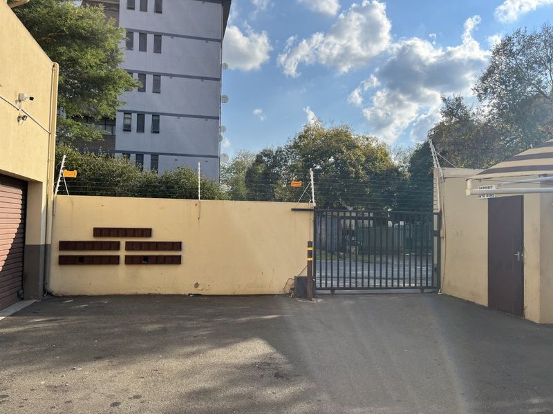Exterior view of the apartment complex entrance featuring a secure gated access point, perimeter wall with electric fencing, and communal post boxes.