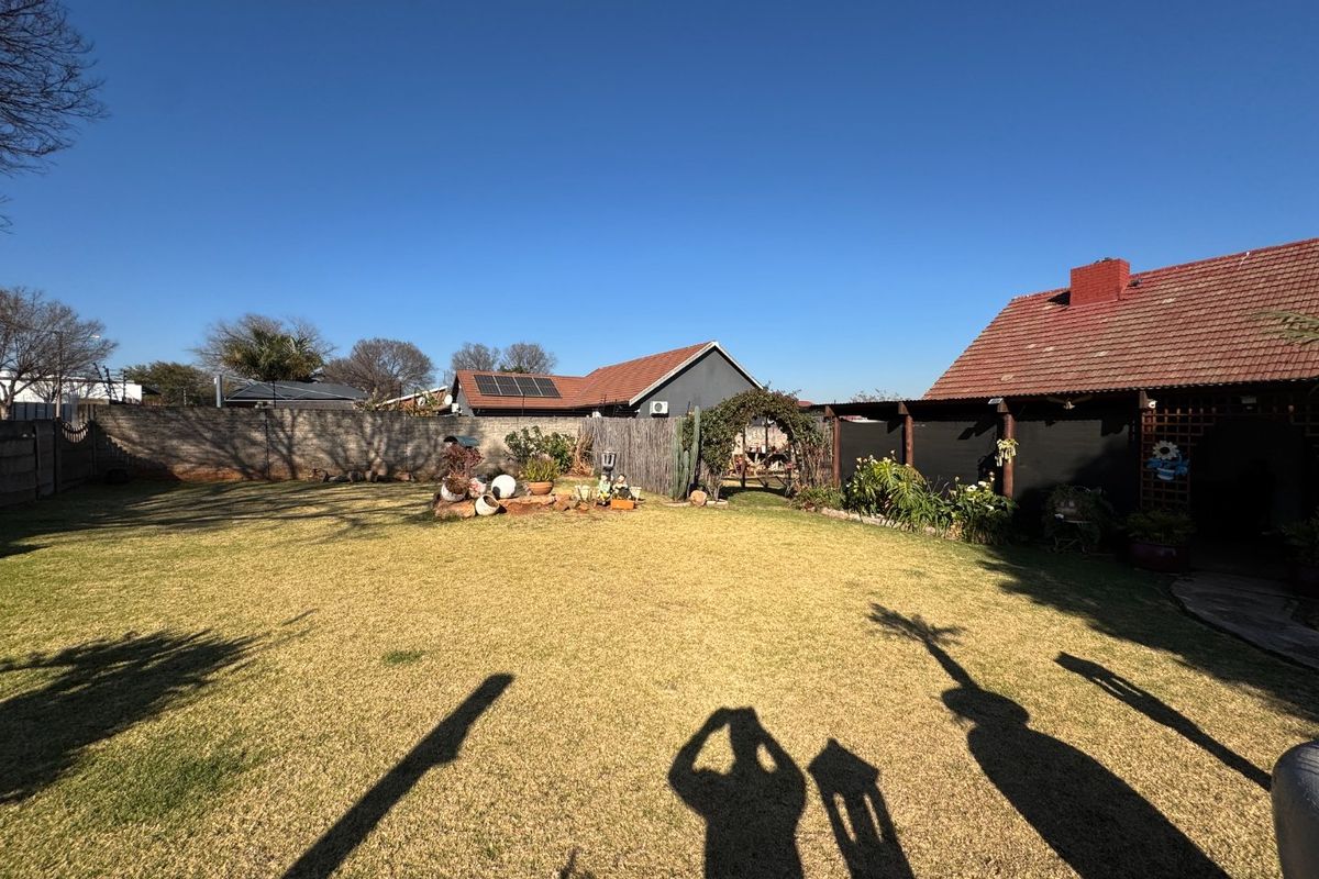 A spacious rear garden featuring a well-maintained lawn, perimeter walling, and a covered patio area attached to the main house structure.