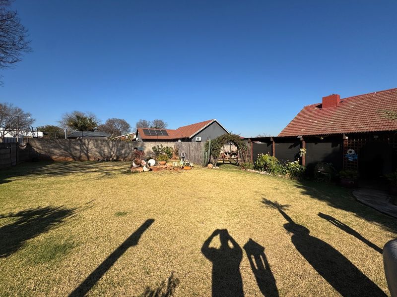A spacious rear garden featuring a well-maintained lawn, perimeter walling, and a covered patio area attached to the main house structure.