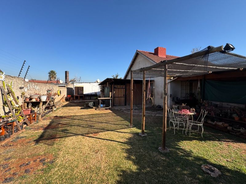 Rear garden area featuring a lawn, brick boundary wall with electric fencing, and a timber pergola structure providing shaded outdoor space.