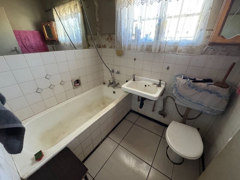 A dated bathroom featuring a standard bathtub, wall-mounted basin, and toilet with original tiled finishes, requiring modernization and cosmetic updates.