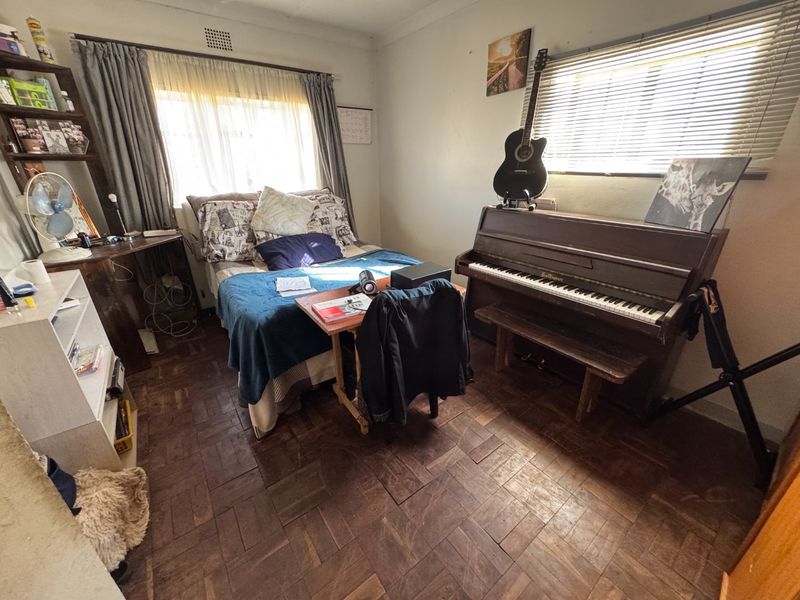 A bedroom featuring classic parquet flooring, natural light through venetian blinds, and neutral wall finishes, offering a functional space with potential for modernization.