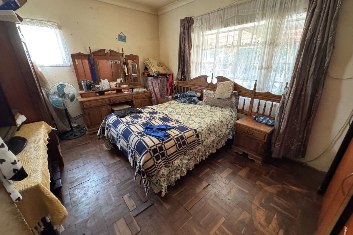 A bedroom featuring original parquet flooring and large windows, requiring cosmetic updates and refurbishment to restore its appeal.