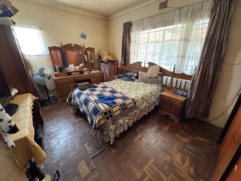 A bedroom featuring original parquet flooring and large windows, requiring cosmetic updates and refurbishment to restore its appeal.