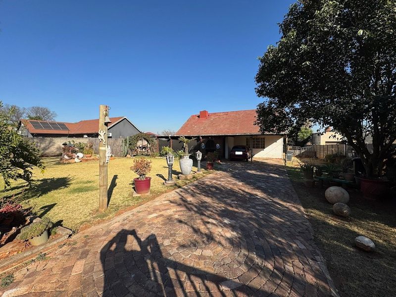 Front view of the property featuring a circular brick paved driveway leading to a covered carport and a tiled roof house.